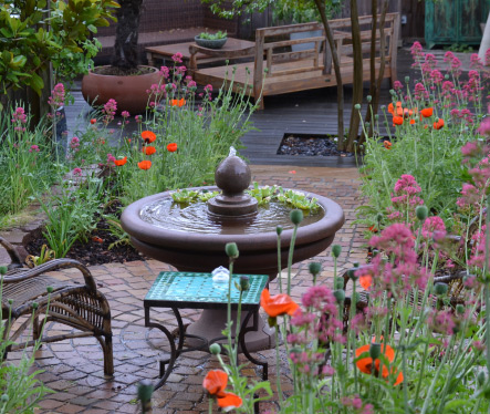 Ziergarten mit Wasserspiel, üppigen Blumenbeeten und gestalteten Gartenwegen.
