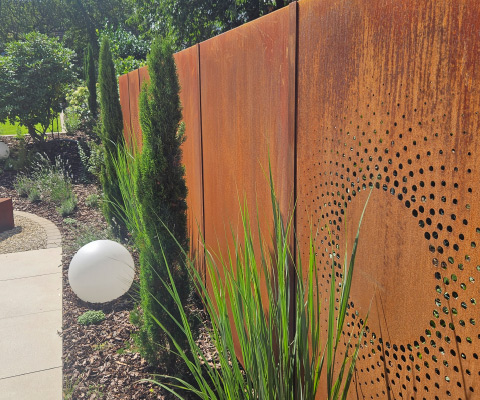 Design-Sichtschutz aus Cortenstahl mit perforiertem Muster und stilvoller Gartengestaltung.