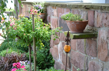 Natursteinmauer im Garten mit integrierter Ablage, Pflanzgefäßen und dekorativer Bepflanzung.