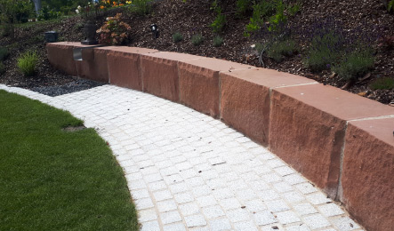 Geschwungene Mauer als Einfassung entlang eines gepflasterten Gartenwegs.
