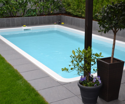 Rechteckiger Pool mit umlaufender Terrasse und präzise verlegten Platten im Garten.