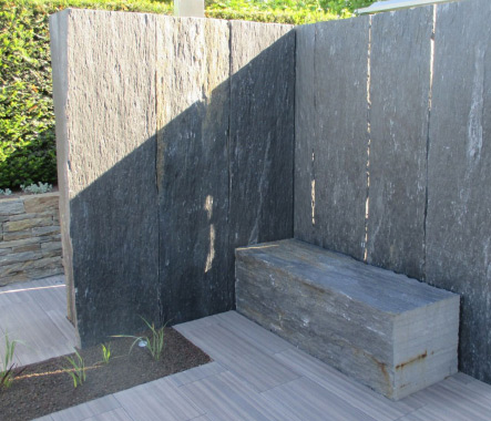 Design-Sichtschutz aus Naturstein mit Sitzblock als stilvolles Element im Garten.