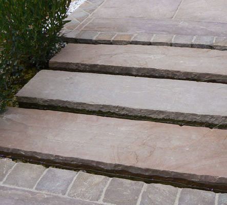 Gartenanlage mit Naturstein-Stufen und präzise verlegten Pflasterflächen.