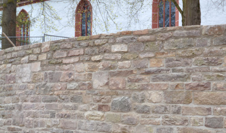 Hochwertige Natursteinmauer mit sauber gesetztem Mauerwerk im Außenbereich einer Kirche.