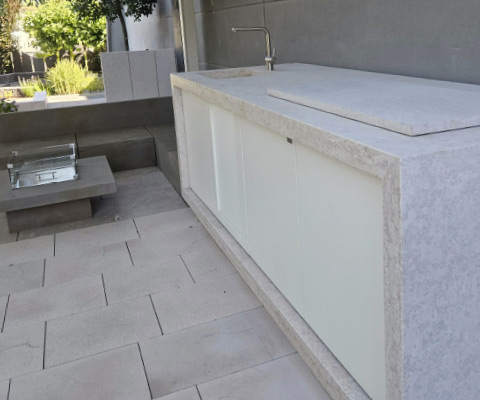 Moderne Outdoorküche im Garten mit Arbeitsfläche, Spüle und integrierter Sitzgelegenheit.