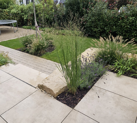 Terrasse mit großformatigem Plattenbelag, Naturstein-Einfassung und integrierter Bepflanzung im Garten.