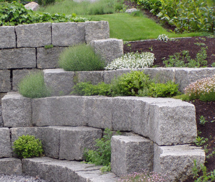 Gestufte Natursteinmauer zur Terrassierung mit integrierter Bepflanzung im Garten.