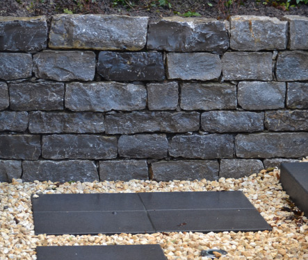 Naturstein-Trockenmauer im Garten mit sauberer Einfassung, Kiesfläche und Trittplatten.
