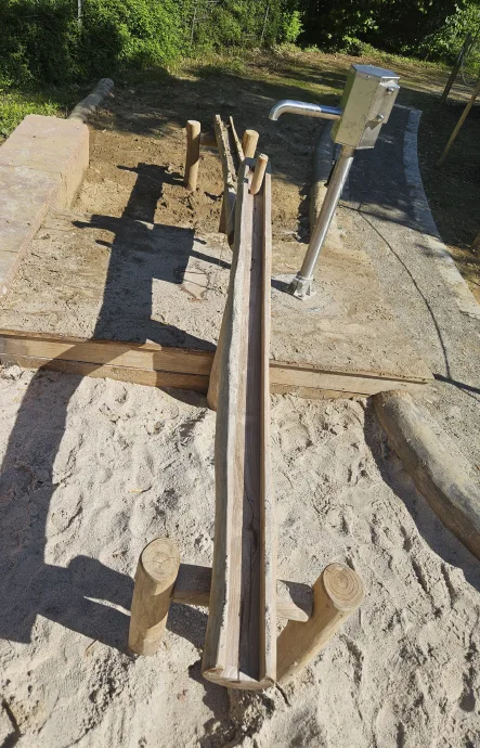 Wasserspiel mit Holzrinne und Wasserpumpe auf einem Spielplatz.