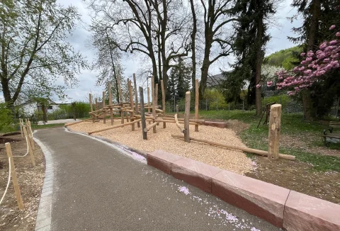Gestaltete Außenanlage mit Weg, Bäumen und Kletteranlage aus Holz.