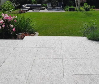 Helle Terrassenfläche aus Natursteinplatten mit Blick in einen begrünten Garten.